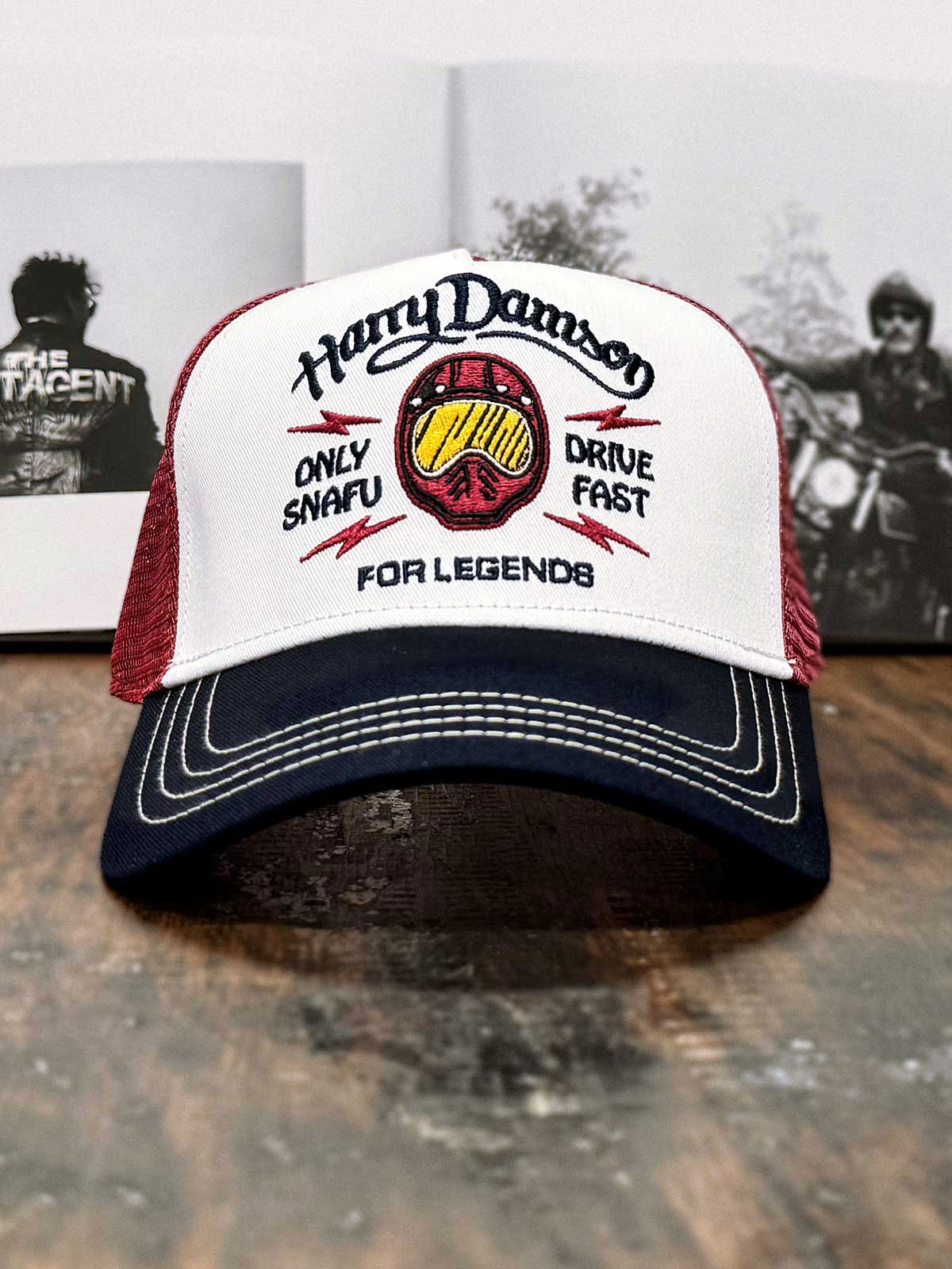 Burgunderfarbene Trucker Cap im Streetwear-Stil, Limited Edition, mit Motorradhelm und 'Only Snafu - Drive Fast' Blitzen, Harry Damson Schriftzug oben, FOR LEGENDS Logo unten, auf Holzstisch