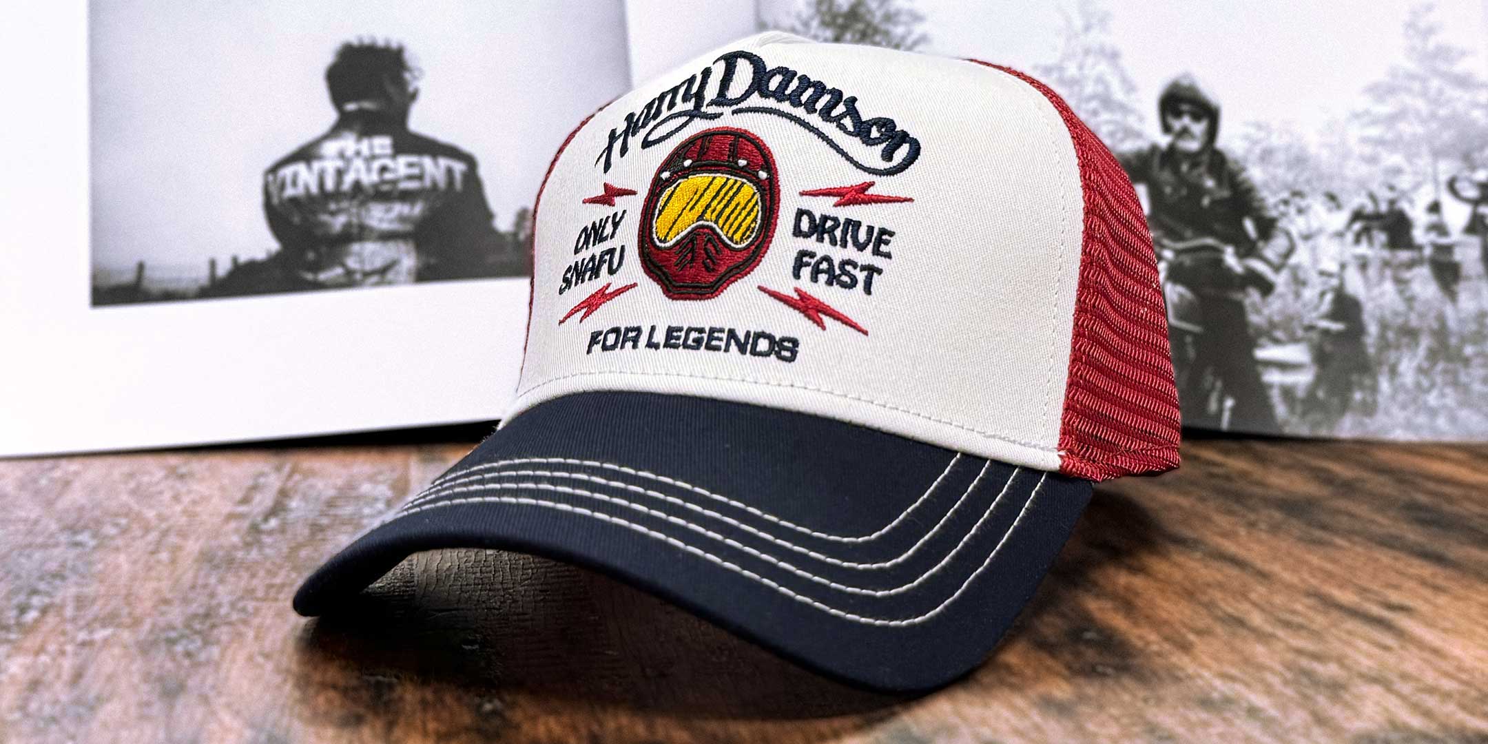Burgunderfarbene Trucker Cap in schräger Ansicht von links, mit Fokus auf 'Drive Fast' Schriftzug und Motorradhelm im Hintergrund, For Legends x Harry Damson