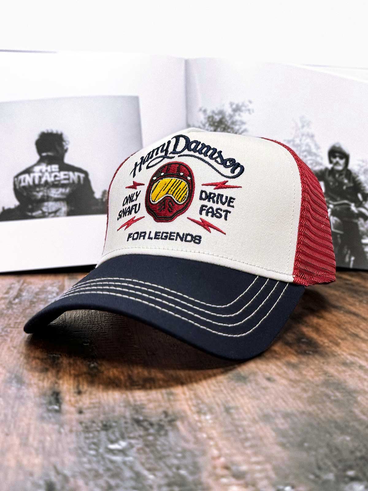 Burgunderfarbene Trucker Cap von der linken Seite mit vintage schwarz-weißem Buch im Hintergrund, For Legends x Harry Damson