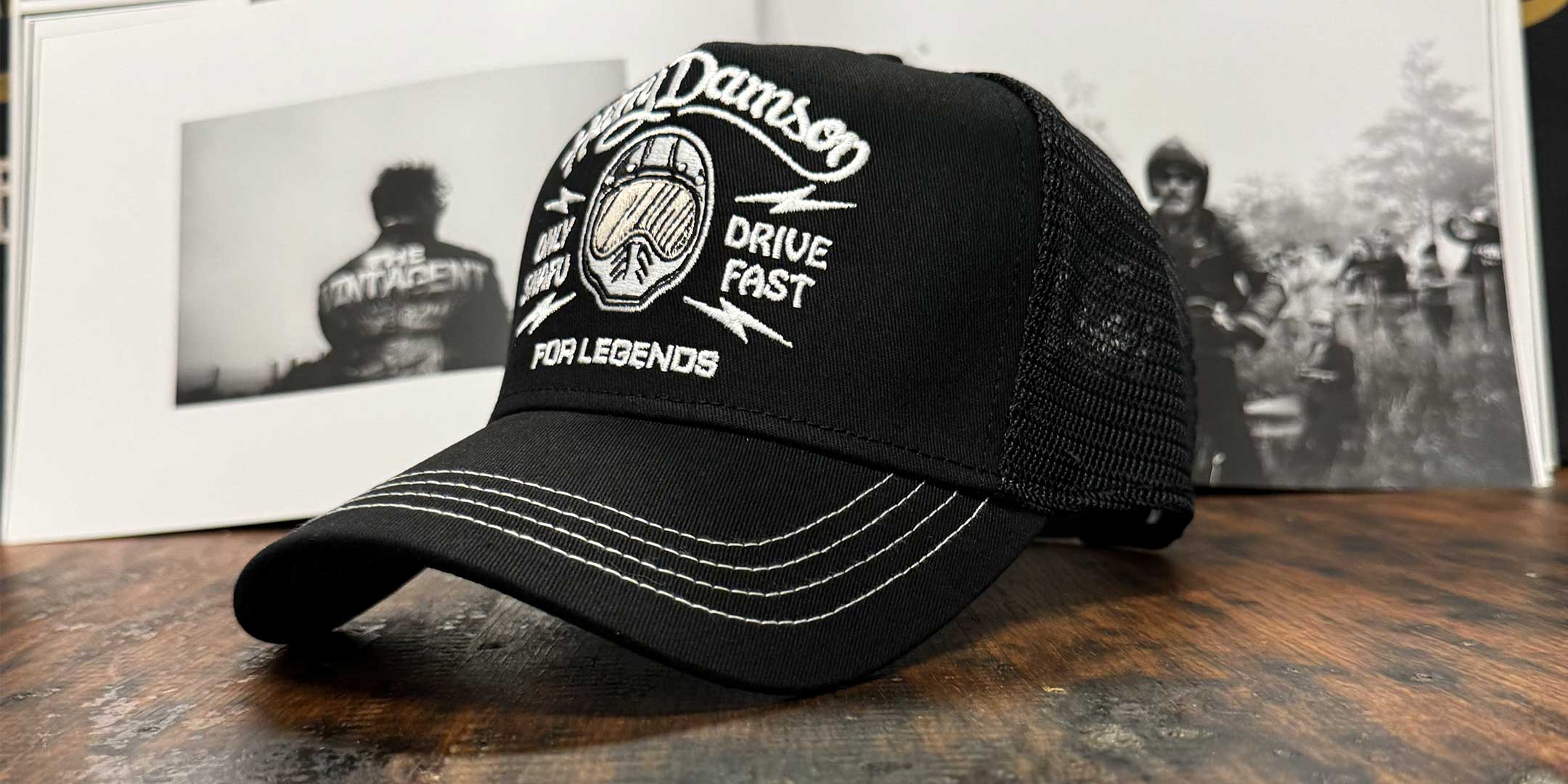 Schwarze Trucker Cap im Streetwear-Look mit Frontansicht, Motorradfahrer im Hintergrund, For Legends x Harry Damson