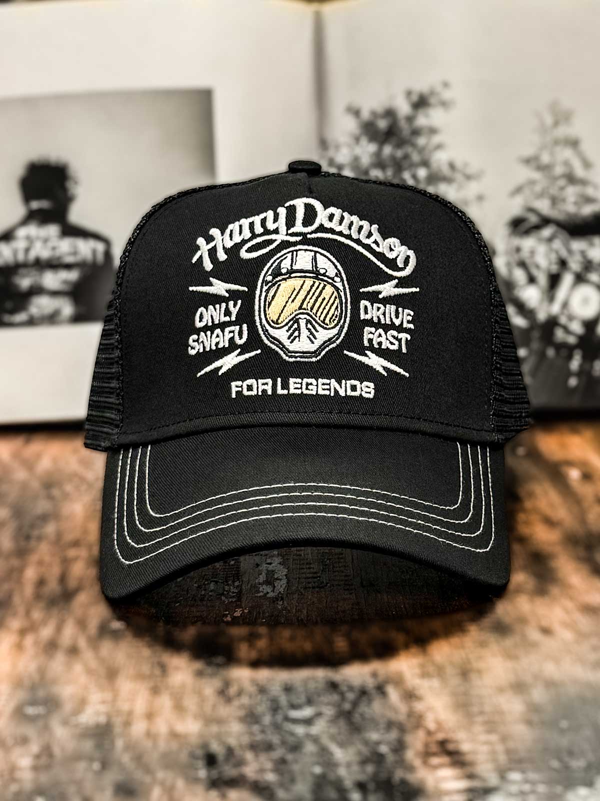 Schwarze Trucker Cap im Streetwear-Stil, Limited Edition, mit Motorradhelm und 'Only Snafu - Drive Fast' Blitzen, Harry Damson Schriftzug oben, FOR LEGENDS Logo unten, auf HolzstischSchriftzug oben, FOR LEGENDS unten
