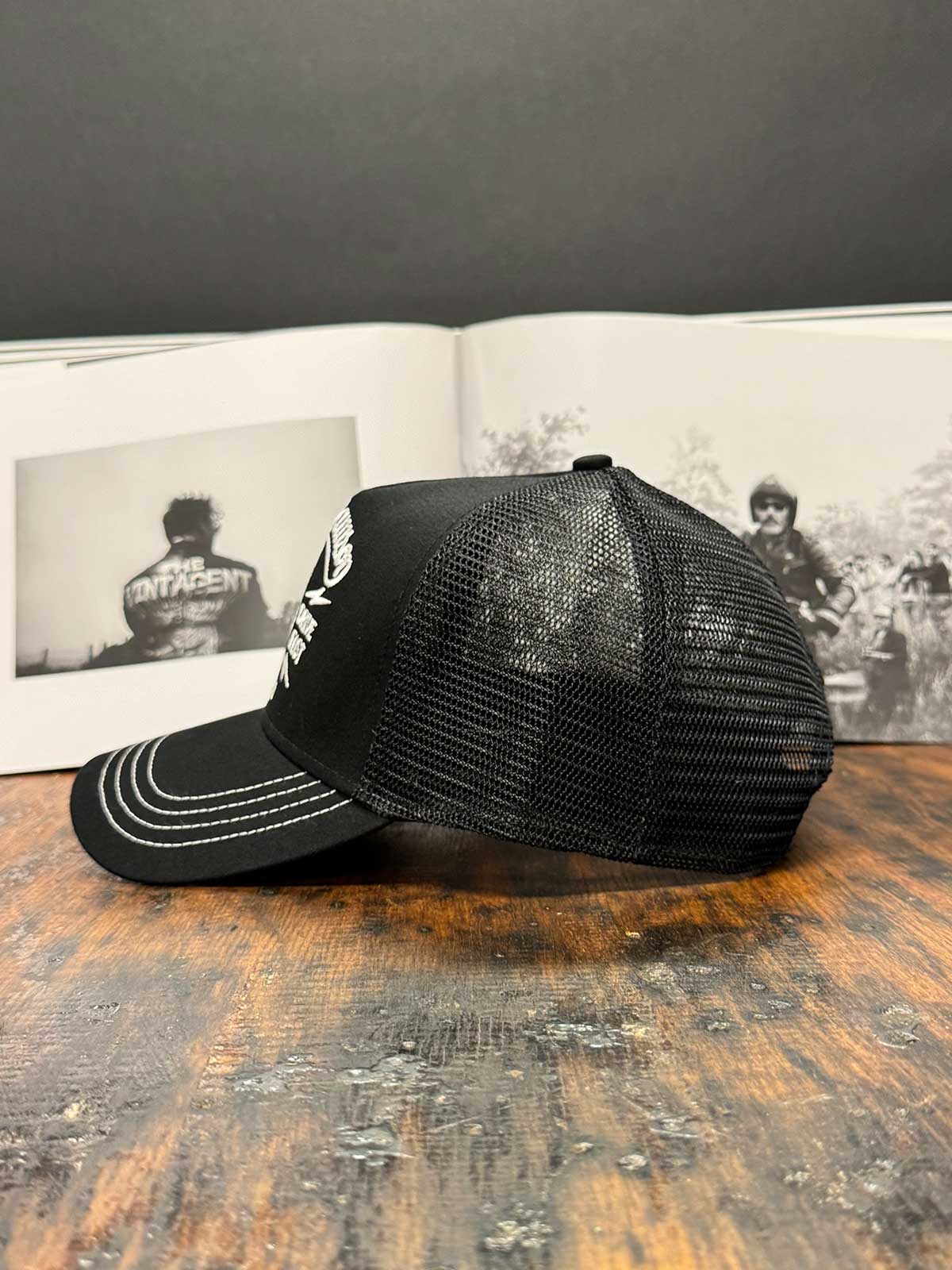 Schwarze Trucker Cap von der linken Seite mit vintage schwarz-weißem Buch im Hintergrund, For Legends x Harry Damson