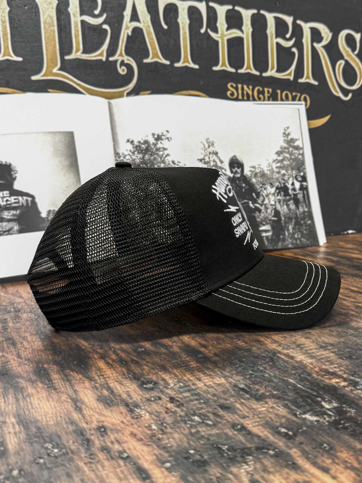 Schwarze Trucker Cap im Streetwear-Stil von der Seite, mit Café Racer Motorrad im Hintergrund, For Legends x Harry Damson
