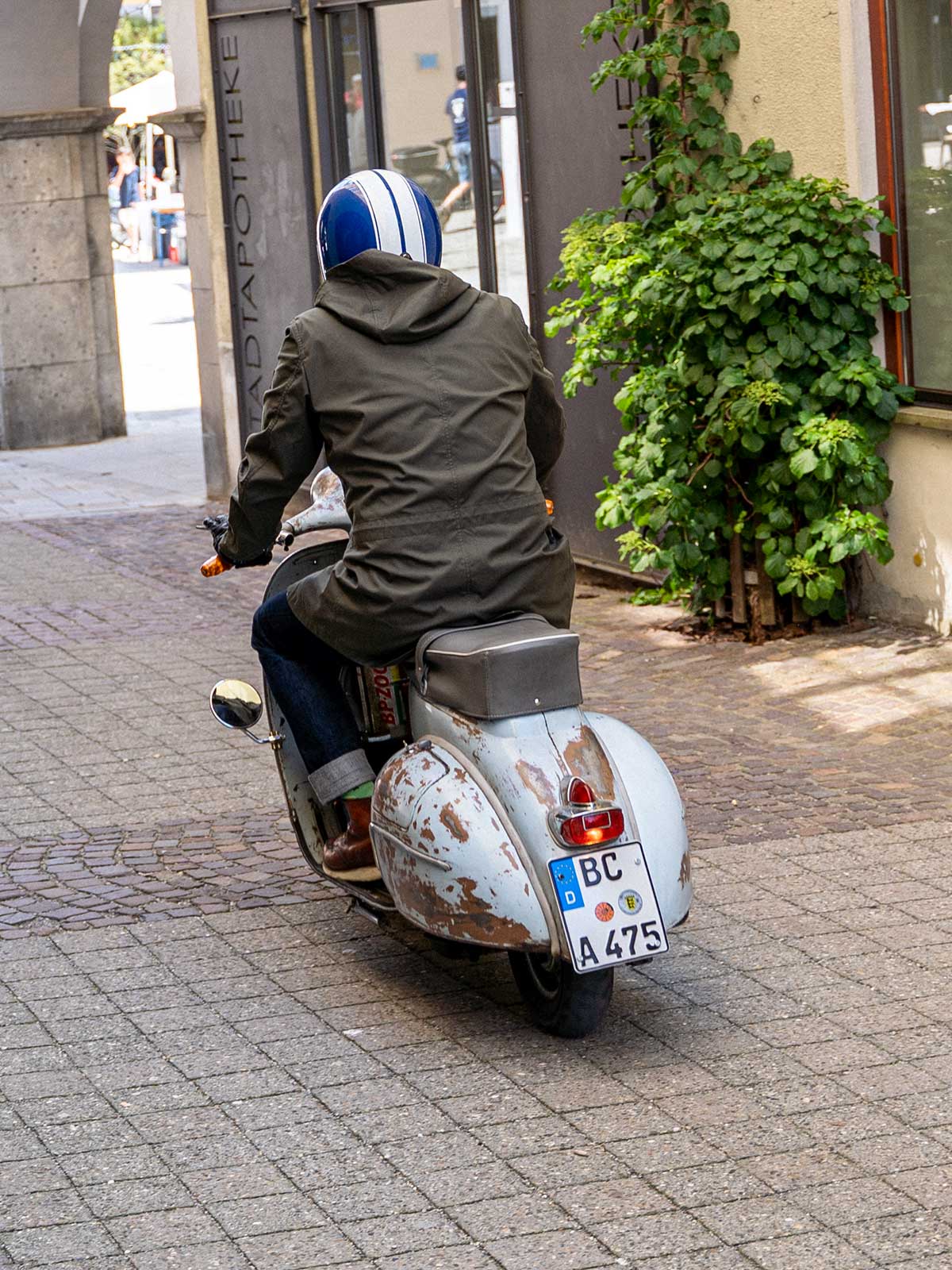 Ein Mann fährt auf einer Vespa | Scooter und trägt einen abriebfesten Parka der Marke For-Legends by Caduff, ideal für urban mobility - for-legends.com. A man rides on a Vespa / Scooter wearing an abrasion-resistant parka by For-Legends by Caduff, ideal for urban mobility - for-legends.com