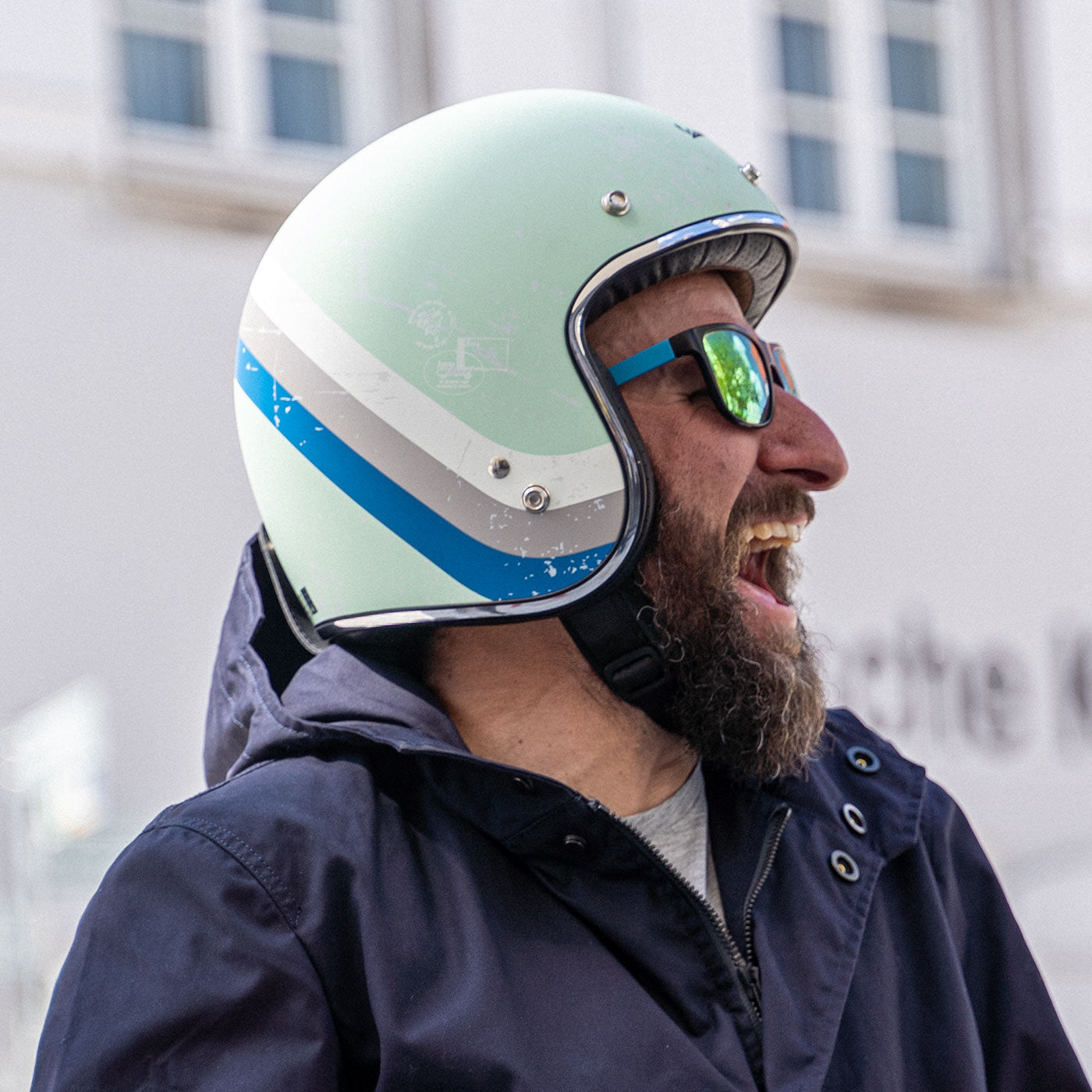Ein Mann sitzt auf einer Vespa, lacht und trägt einen abriebfesten Parka der Marke For-Legends by Caduff, ideal für urban mobility - for-legends.com. A man sits on a Vespa, laughs and wearing an abrasion-resistant parka by For-Legends by Caduff, ideal for urban mobility - for-legends.com.