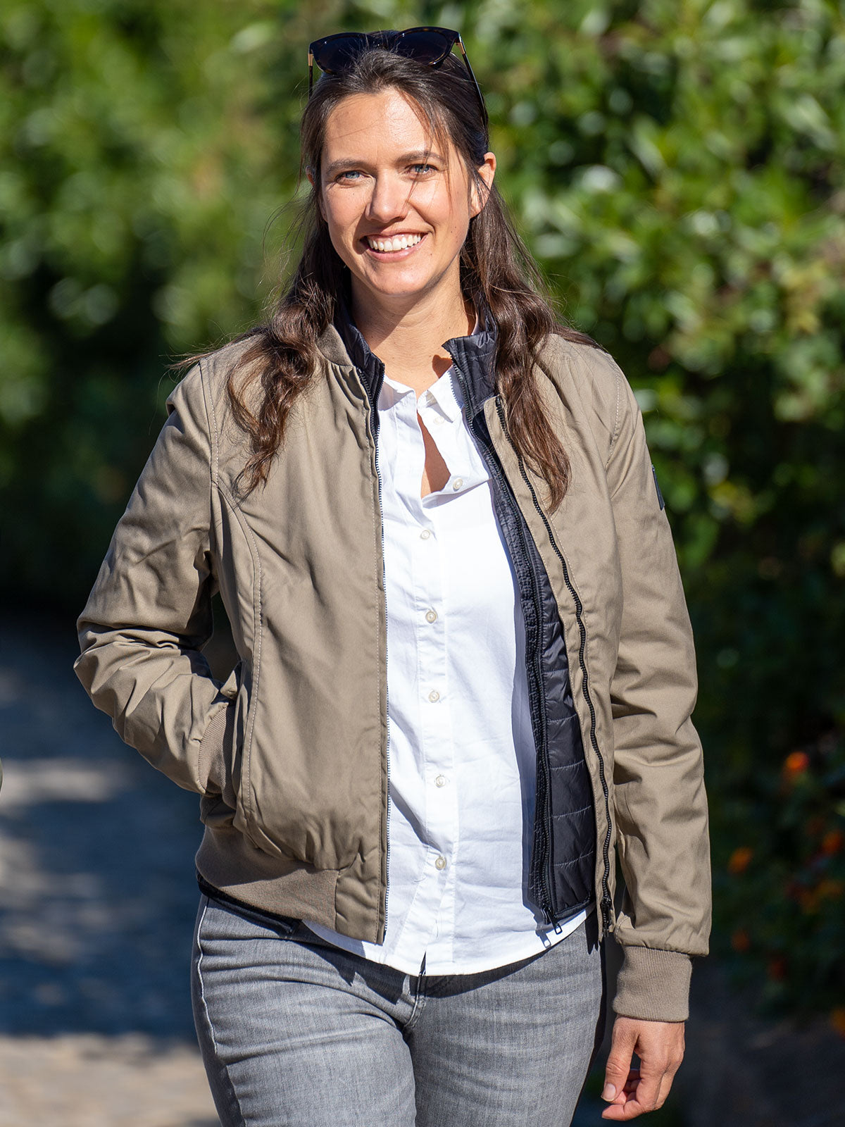 WOMAN MODEL WALKING WITH A SKATEBOARD IN THE CITY WEARING A MUD URBAN MOBILITY BOMBER JACKET FOR LEGENDS BY CADUFF