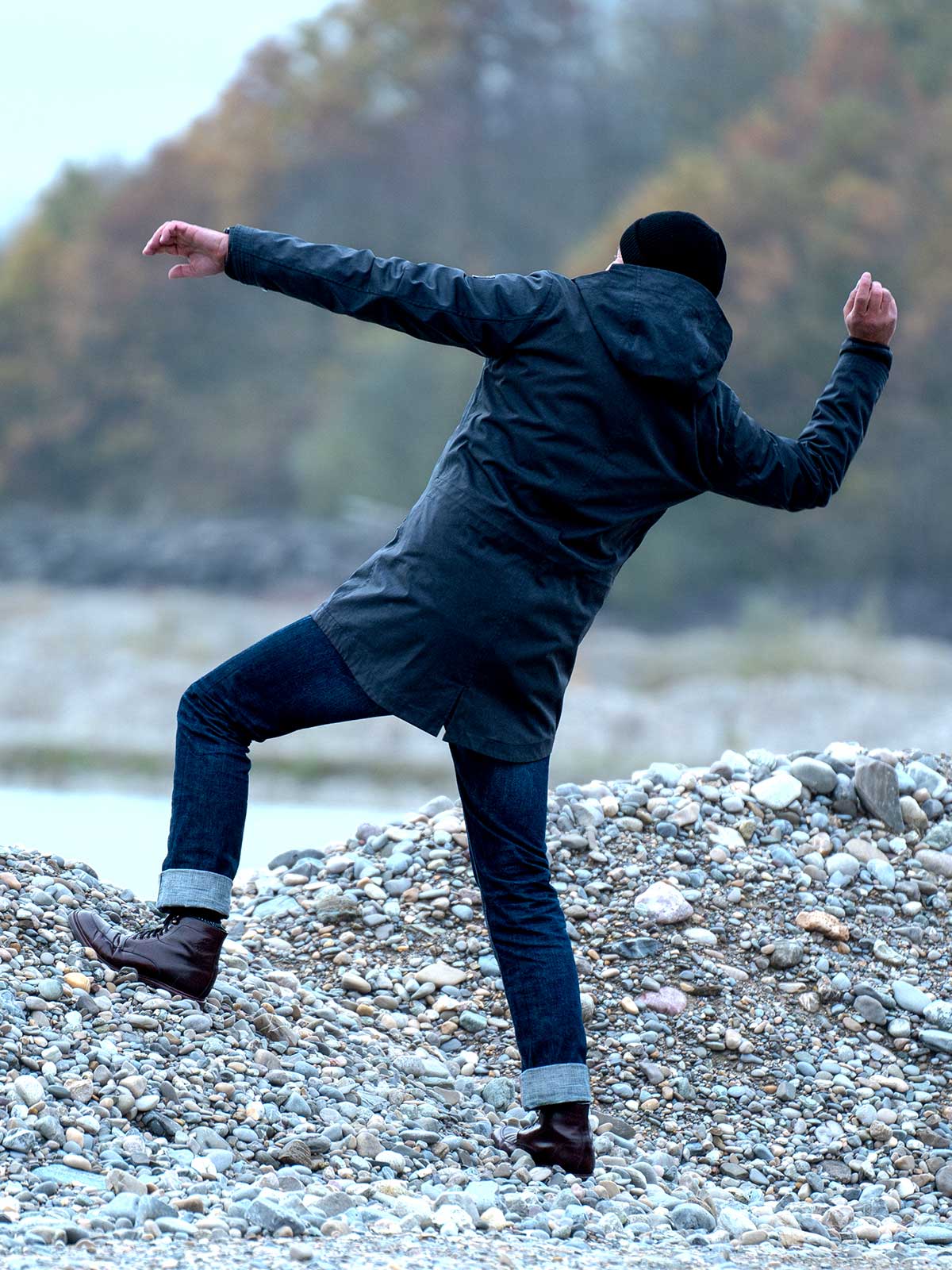 Model wearing a premium winter parka for men from for-legends.com by Caduff, crafted from exclusive high-density knit Japanese fabric, standing in a rocky winter landscape in the background a Land Rover Defender. / Modell trägt einen hochwertigen Winterparka für Herren von for-legends.com by Caduff aus einem exklusivem High-Density-Jersey aus Japan, stehend in einer felsigen Winterlandschaft im Hintergrund ein Landrover Defender.