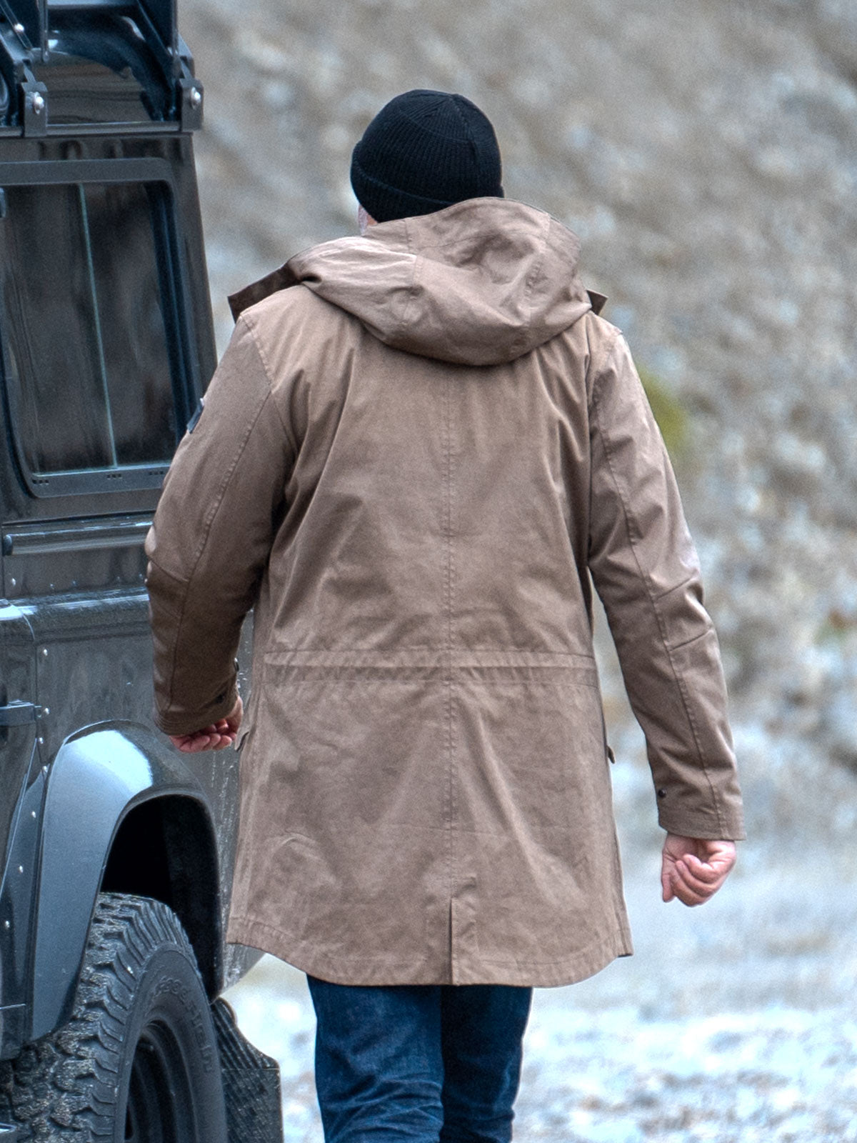 Model wearing a premium winter parka for men from for-legends.com by Caduff, crafted from exclusive high-density knit Japanese fabric, standing in a rocky winter landscape in the background a Land Rover Defender. / Modell trägt einen hochwertigen Winterparka für Herren von for-legends.com by Caduff aus einem exklusivem High-Density-Jersey aus Japan, stehend in einer felsigen Winterlandschaft im Hintergrund ein Landrover Defender.