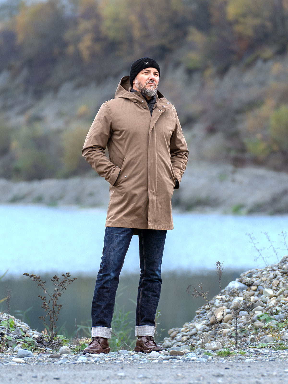 Model wearing a premium winter parka for men from for-legends.com by Caduff, crafted from exclusive high-density knit Japanese fabric, standing in a rocky winter landscape in the background a Land Rover Defender. / Modell trägt einen hochwertigen Winterparka für Herren von for-legends.com by Caduff aus einem exklusivem High-Density-Jersey aus Japan, stehend in einer felsigen Winterlandschaft im Hintergrund ein Landrover Defender.