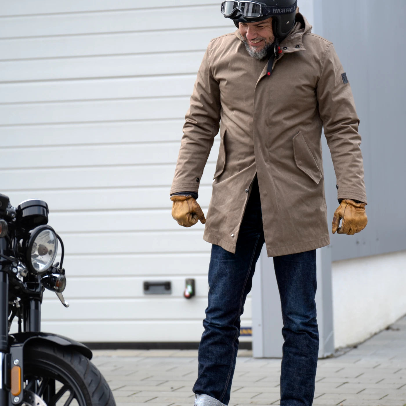 Model in the Salute Blue CADUFF 2-in-1 Winter Parka standing beside a Harley motorcycle; YKK METALUX® two-way zipper opened from the bottom for comfortable urban commuting.