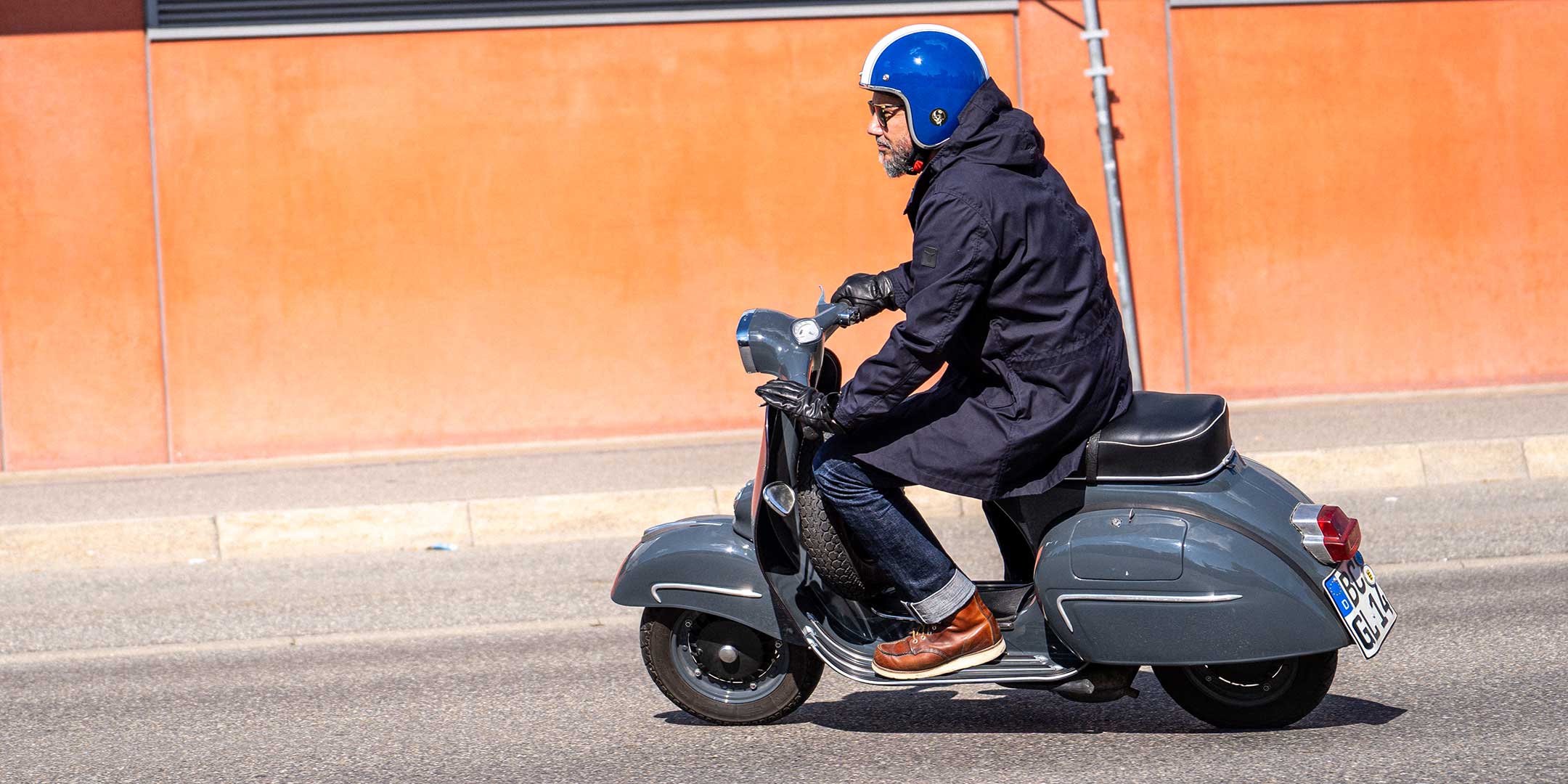 Ein Mann fährt auf einer Vespa | Scooter und trägt einen abriebfesten Parka der Marke For-Legends by Caduff sowie einen Back Protector von Orthema, ideal für urban mobility - for-legends.com. A man rides on a Vespa / Scooter wearing an abrasion-resistant parka by For-Legends by Caduff and a Back Protector from Orthema ideal for urban mobility - for-legends.com