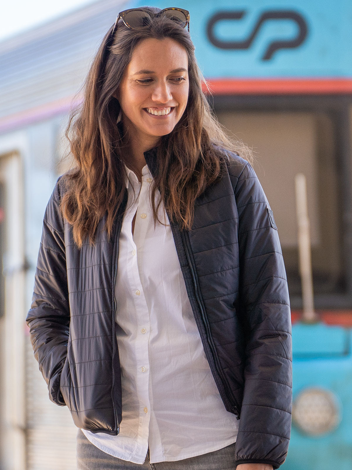 WOMAN MODEL STANDING IN THE TRAINSTATION IN FRONT OF A TRAIN  WEARING A ECO DOWN INSULATION JACKET WITH 100% RECYLED FIBRES FROM PET BOTTLES